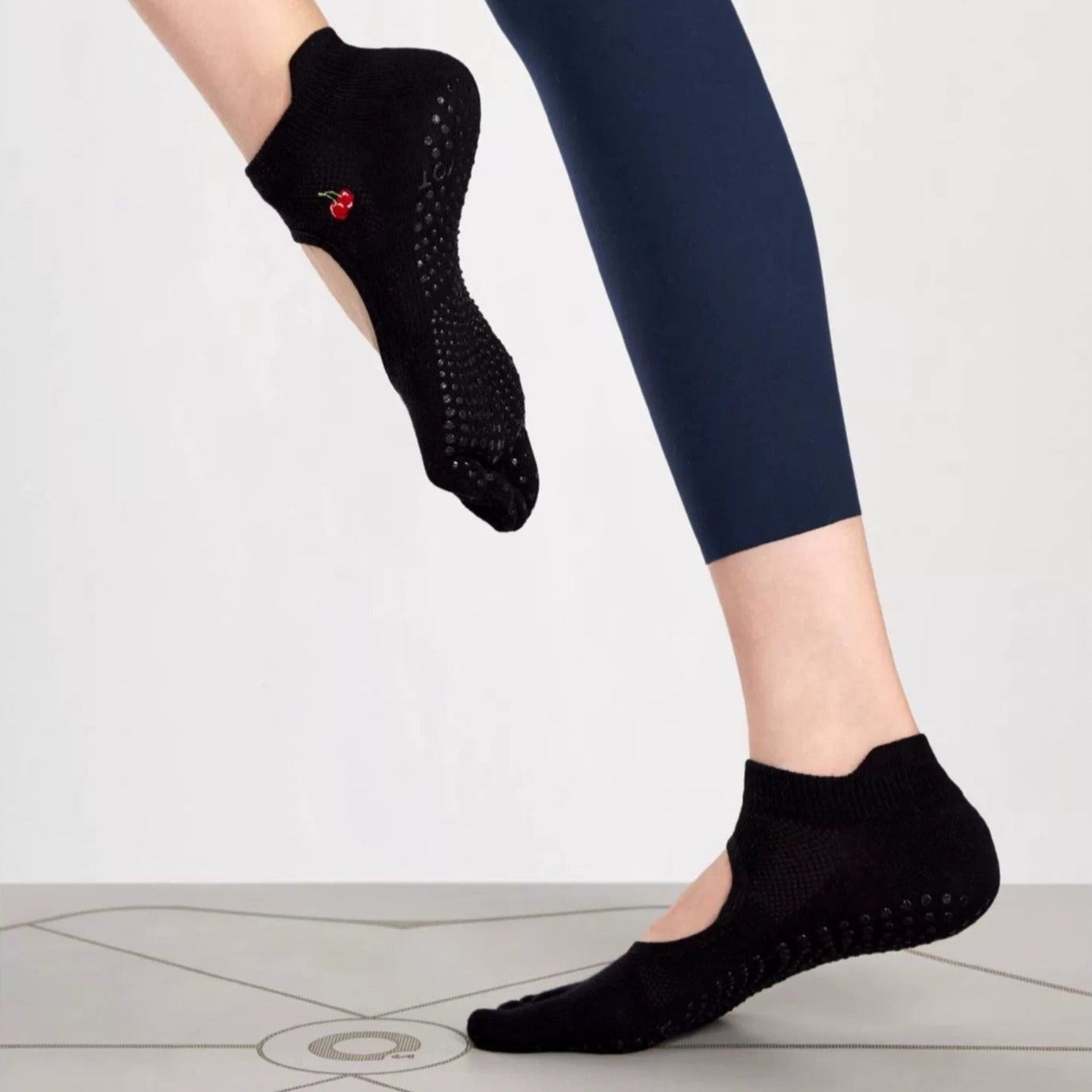 A pair of brown toeless non-slip grip socks with a pattern of white circles on the sole and a red cherry on the ankle support band.